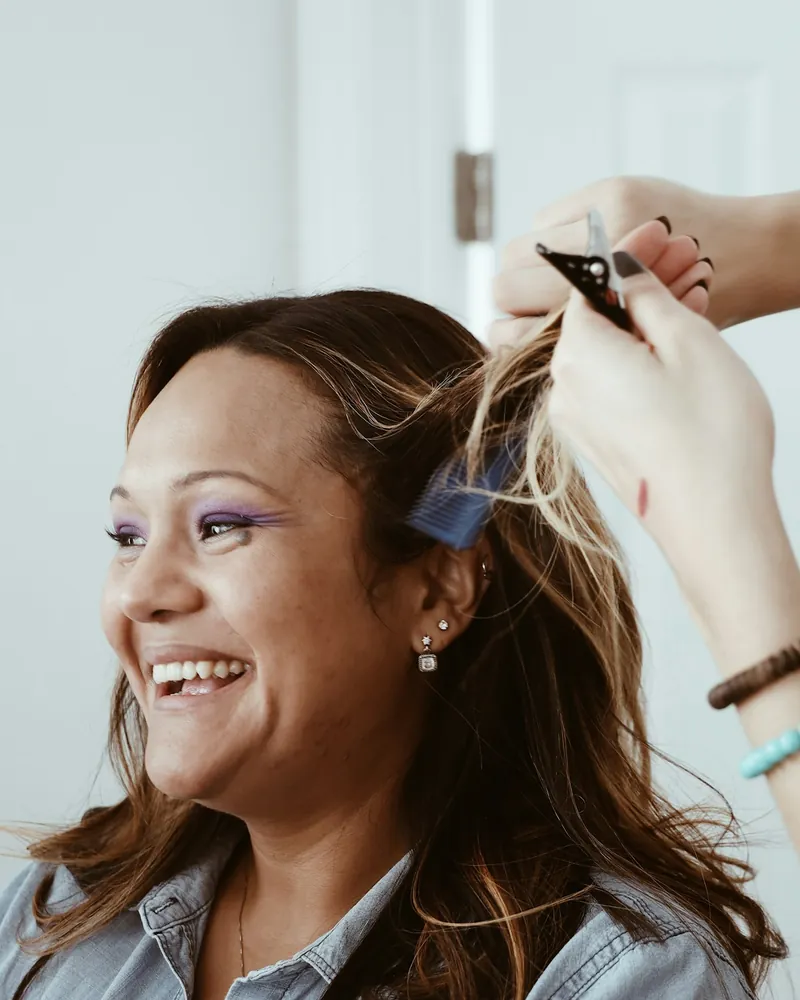 Woman laughing in a hair salon chair while her stylist works